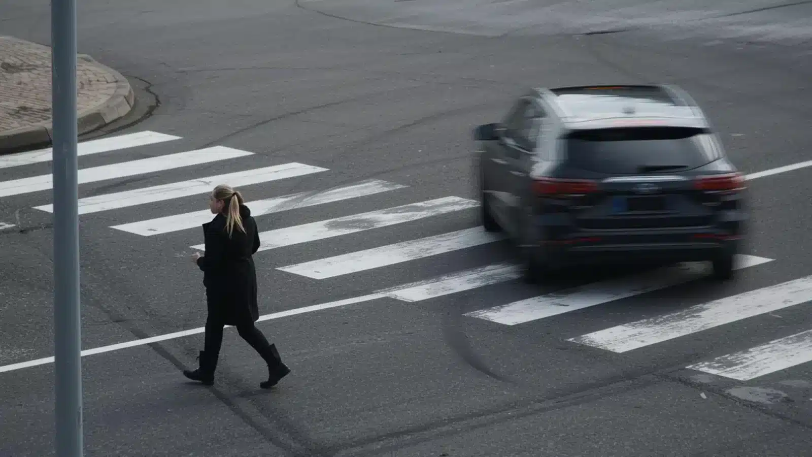 A woman walks across a crosswalk while a blurred SUV drives nearby.
