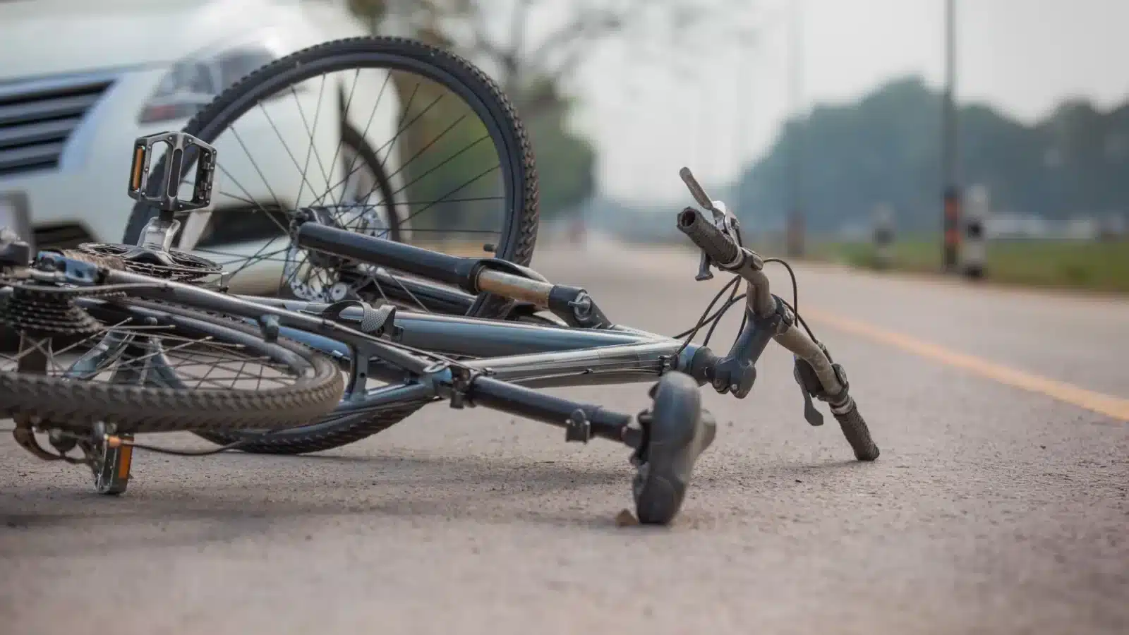 Bicycle lying on its side in the roadway after an accident, with traffic visible in the background.