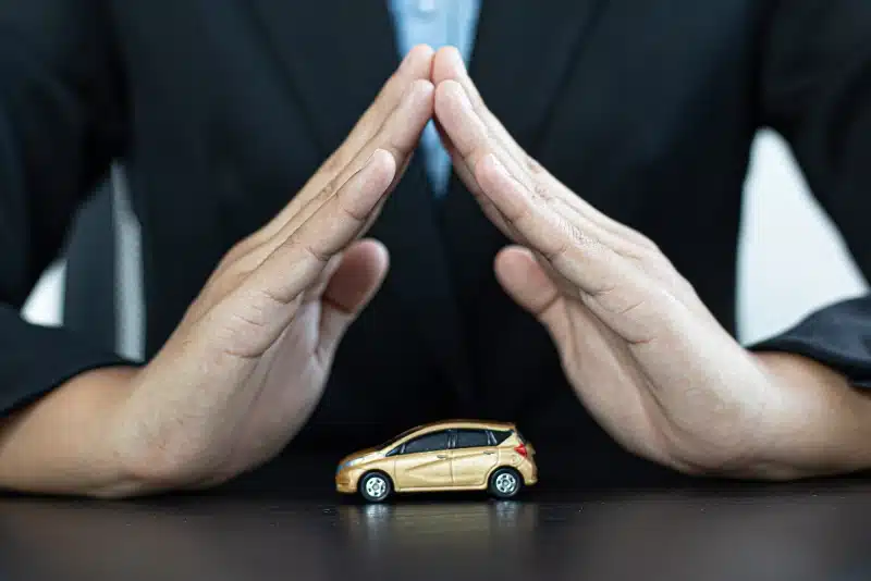 Hands forming a protective shelter over a miniature car, symbolizing car insurance or legal protection.