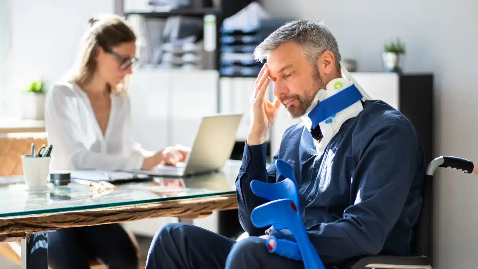 A man in a wheelchair is seated at a desk, working on a laptop with a focused expression.