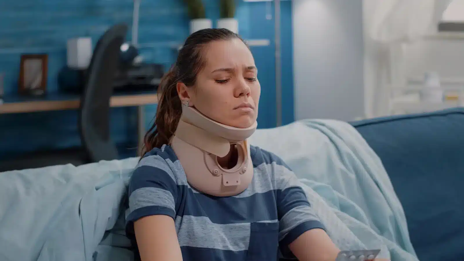 A woman wearing a neck brace sits on a couch, looking contemplative and relaxed in her living room.
